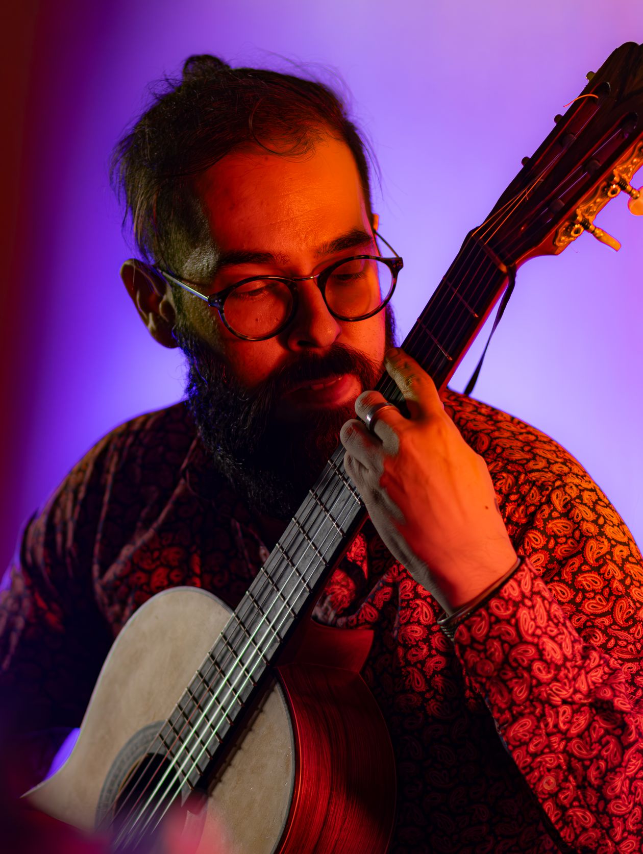 A guitarist concentrating on an acoustic guitar under coloured studio light.
