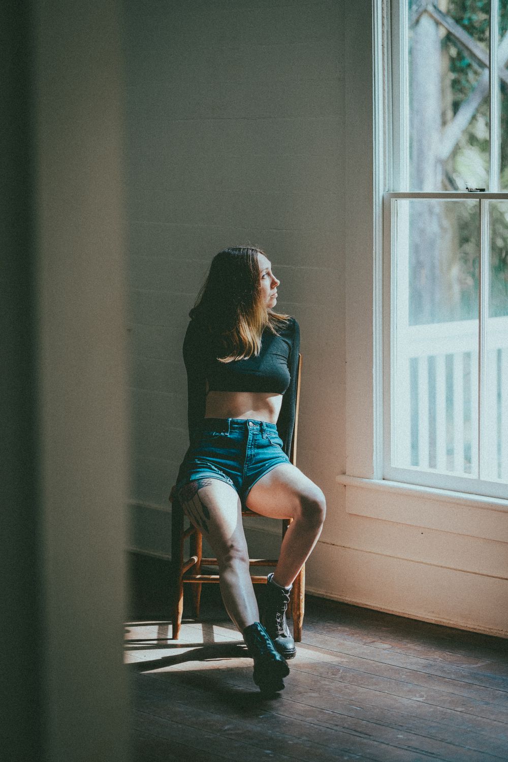 A young woman sitting by a sunlit window in a relaxed pose.