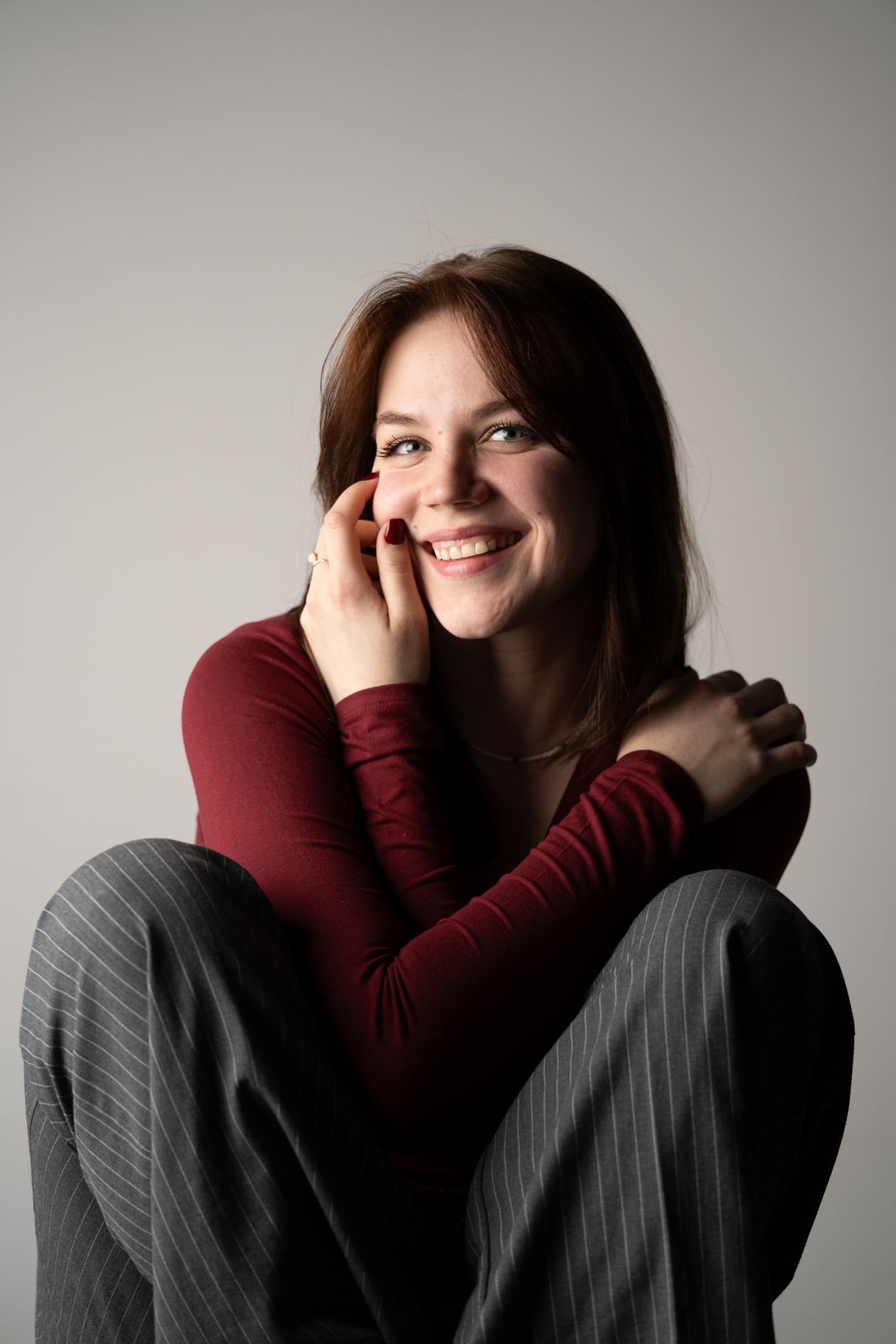A smiling woman in a red sweater resting her cheek on her hand.