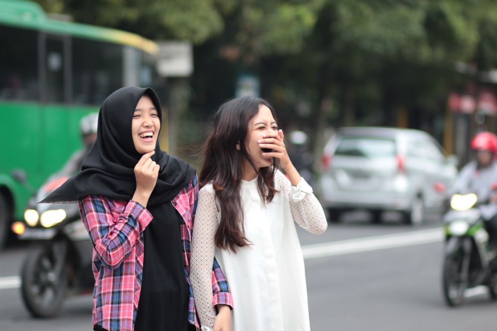 Two young women laughing together on a busy street.