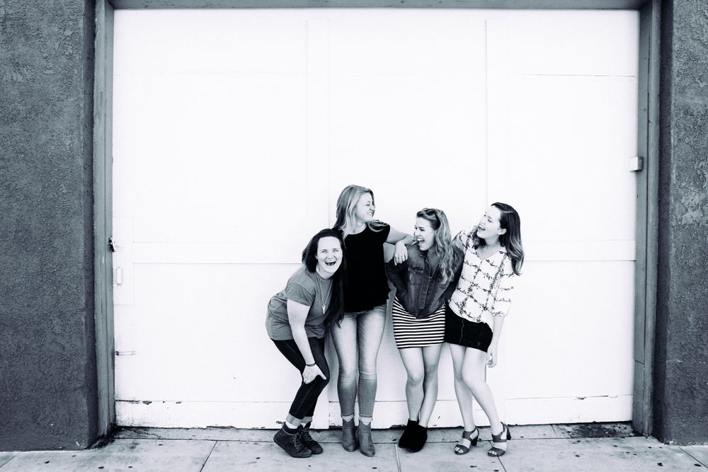 Four friends laughing together in front of a doorway.