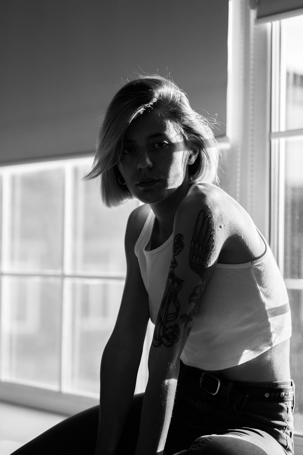 A woman with a tattooed arm sitting by a window, black and white.