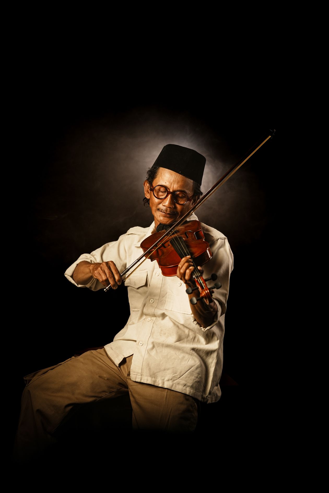 An elderly man playing the violin against a dark background.