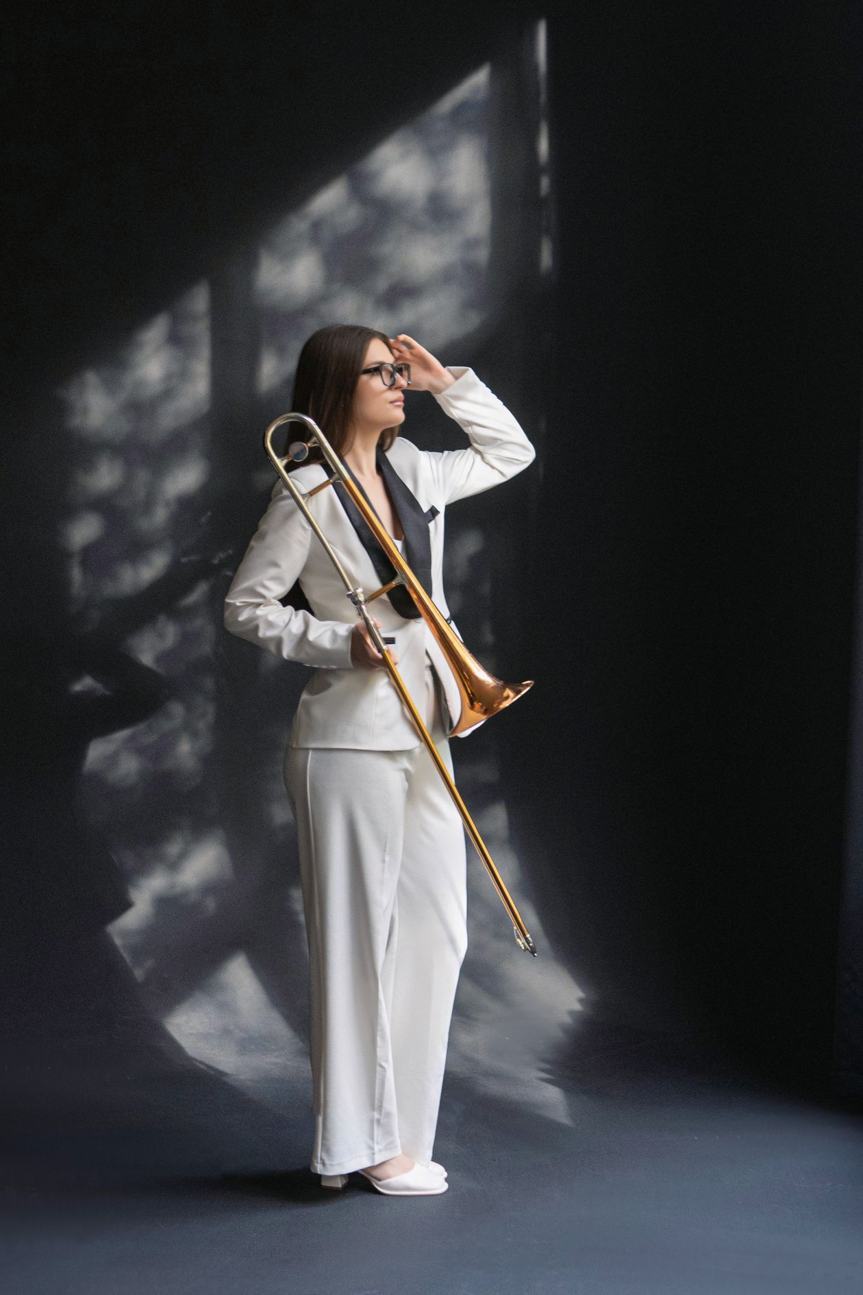 A woman in a white suit holding a trombone in moody light.