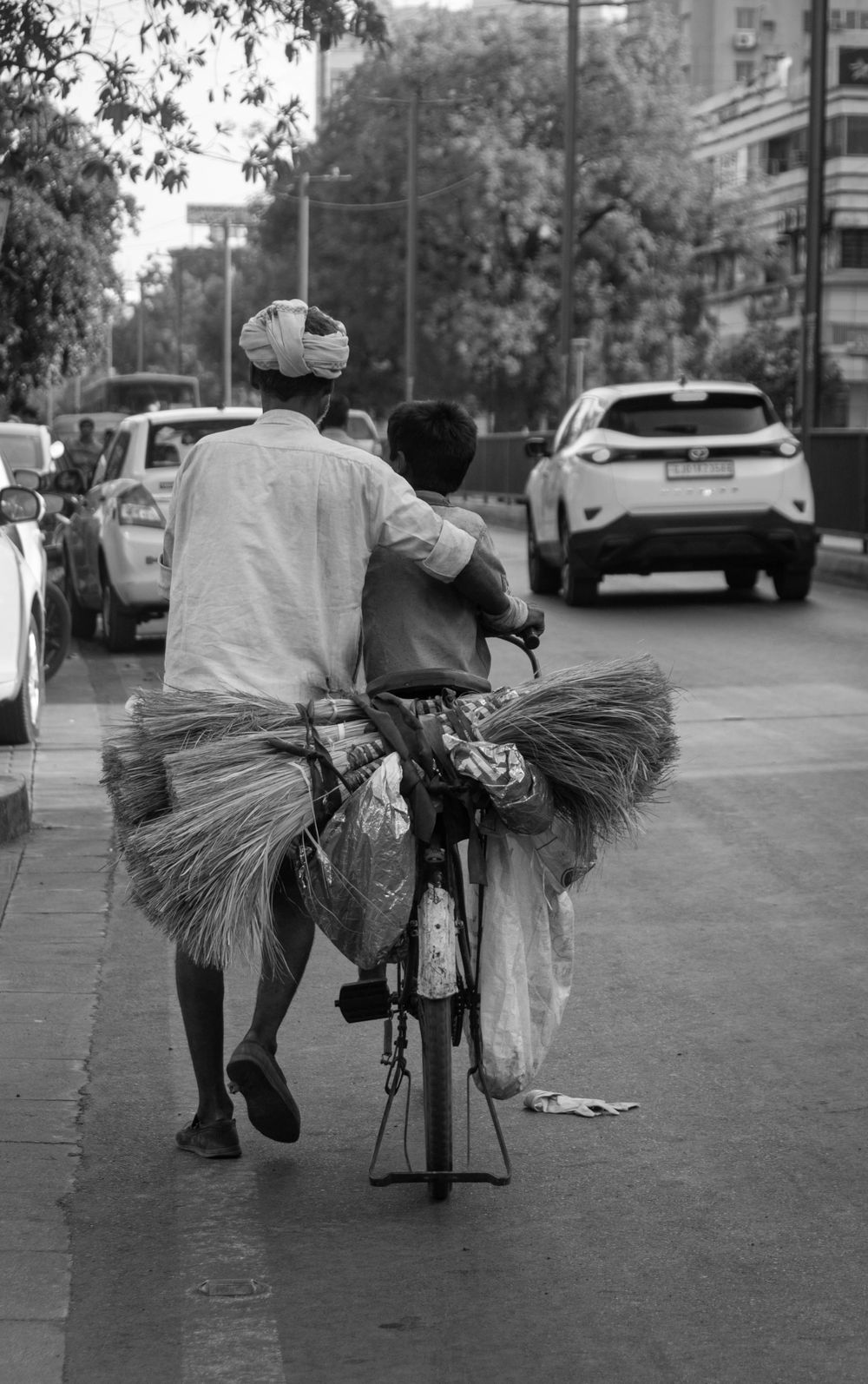 A man cycling with a child on the crossbar down a city street, black and white.