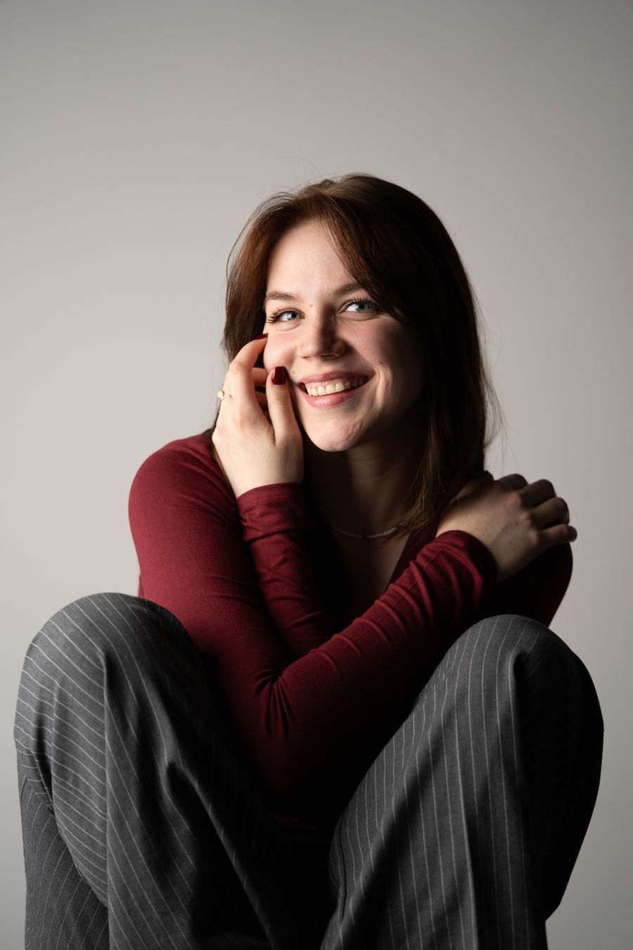 A smiling woman in a red sweater resting her cheek on her hand.