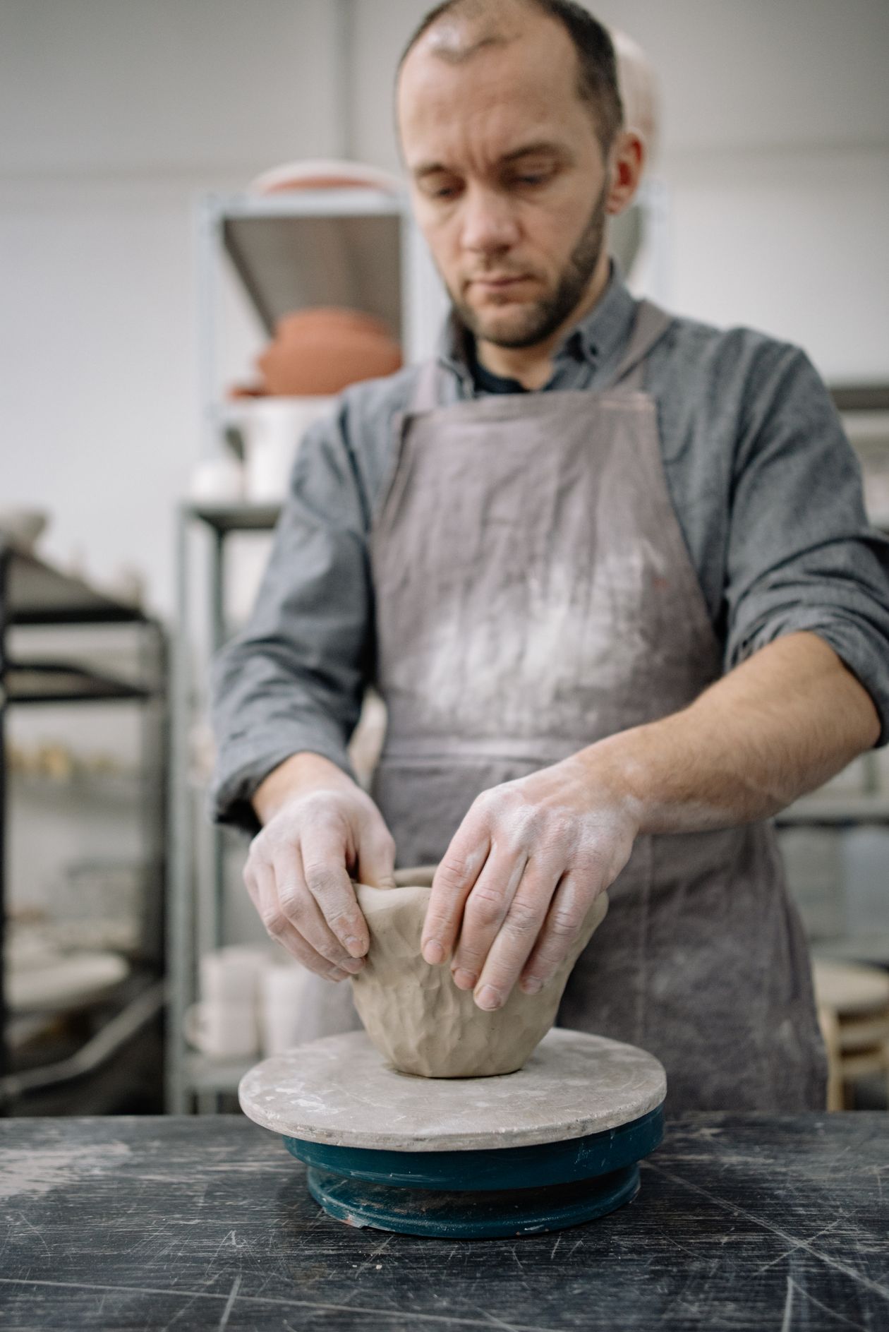 A potter shaping a clay vessel on the wheel in a workshop.