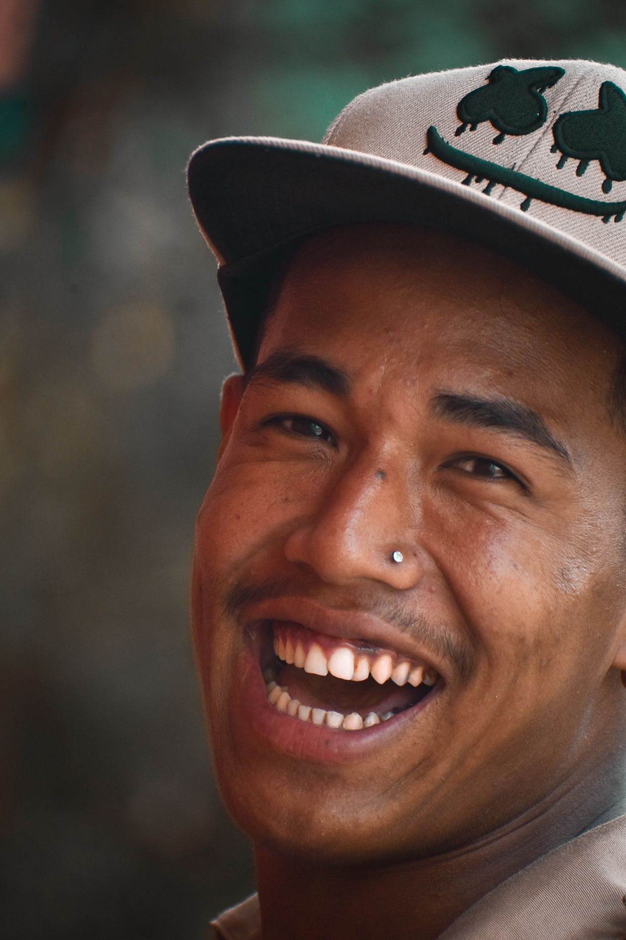 Close-up of a laughing man in a cap with a nose piercing.